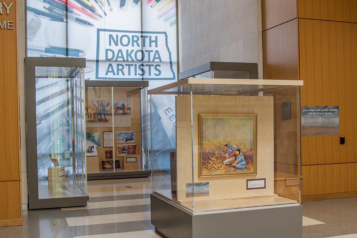A hallway with exhibit cases showcasing paintings by S.D. Nelson
