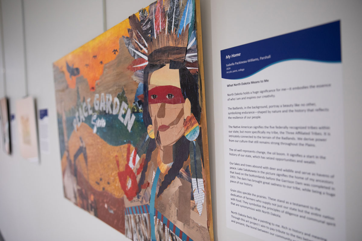Painting by a teenager titled My Home. The painting has a Native American in traditional dress, an oil rig, birds, landscape elements from North Dakota, a red handprint, and says Peace Garden State.