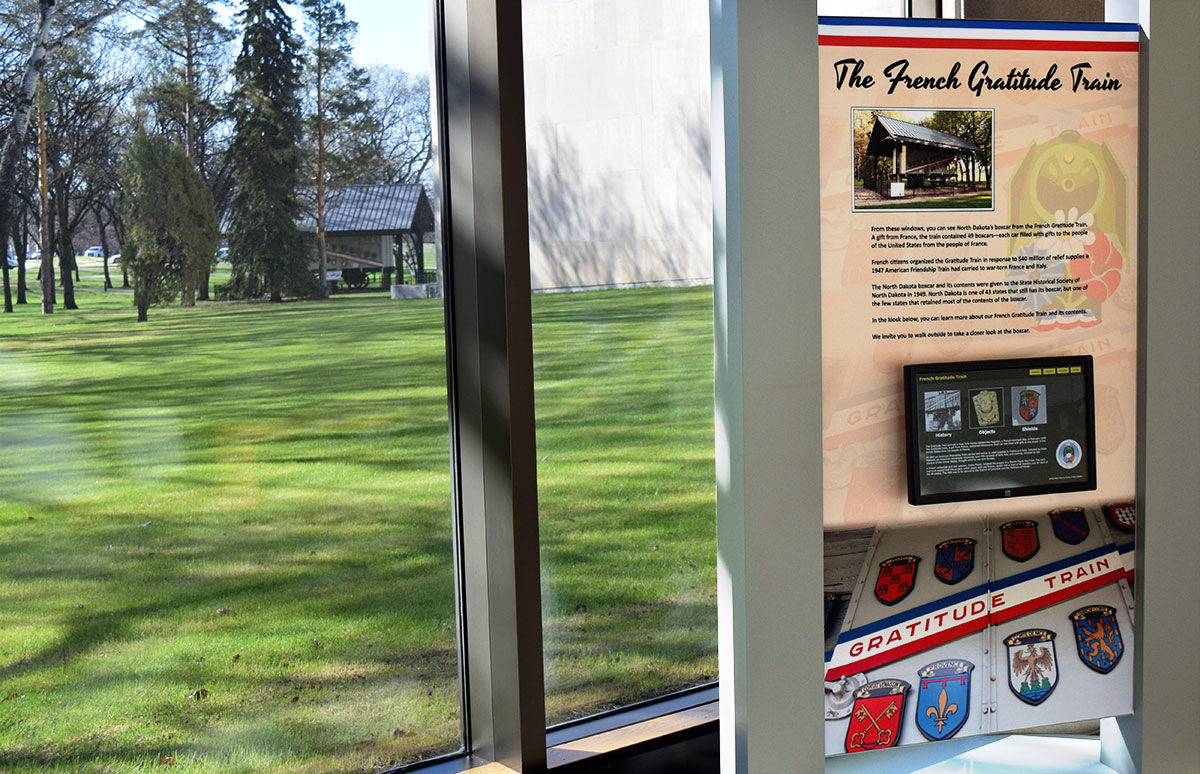 kiosk sitting next to window with outdoor view of green grass and trees and boxcar