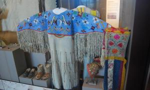 A Native American dress with blue beading on the top and tassles hanging off the arms and some on the body