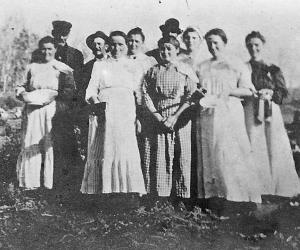 A group of 10 men and women cooks and stewards for a wedding. A couple of the women hold bowls.