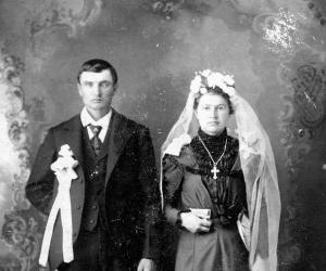 Wedding portrait of a couple. The bride wears white bows at her shoulders and a long ribbon suspended form her waist.